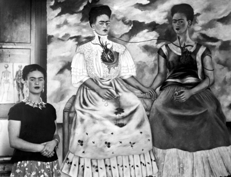 Frida Kahlo shown with her painting Me Twice. The painting shows Kahlo as a 19th century lady linked by an artery to herself. Everett Collection Historical / Alamy Stock Photo