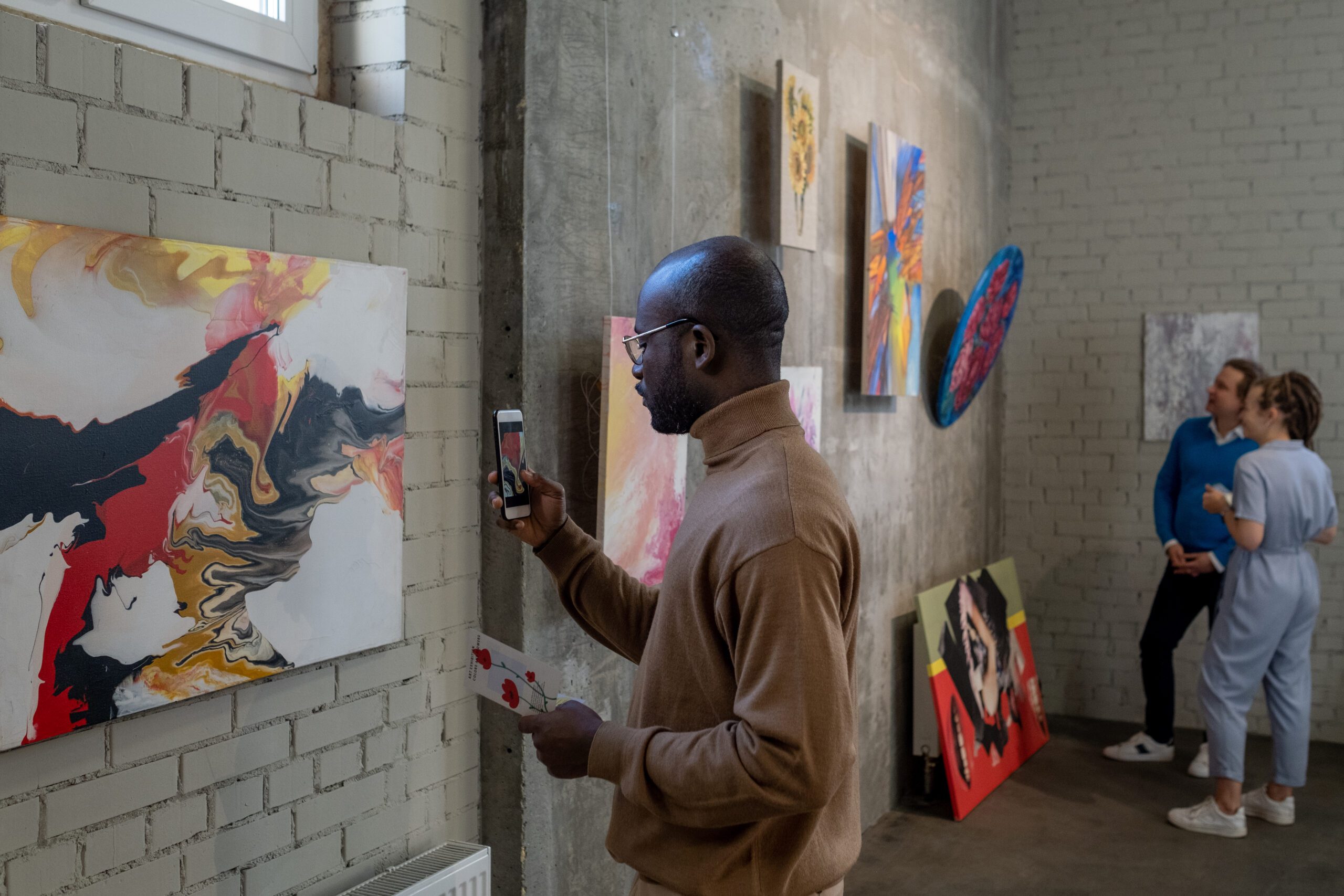 Young Black male visitor of art gallery taking photo of painting